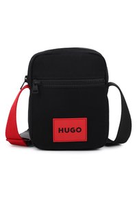 Μαύρη υφασμάτινη τσάντα ταχυδρόμου με κόκκινο λουρί, με μπροστινή τσέπη με φερμουάρ και κόκκινο λογότυπο με το κείμενο "HUGO." Συμπαγής ορθογώνιος σχεδιασμός.