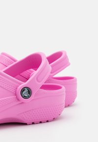 Rosa gummistøvler med en teksturert såle, bakre stropp og ventilasjonshull på siden, som har en sirkulær logoakcent på stroppen.