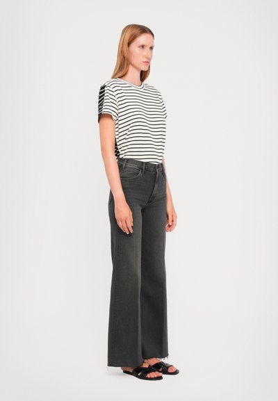 Woman standing wearing a white and black striped short-sleeve shirt, high-waisted dark gray wide-leg jeans, and black sandals.