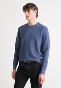 Blåstrikket genser med rund hals, lange ermer og et strukturert mønster. Har en liten logo på brystet og er laget av mykt materiale.