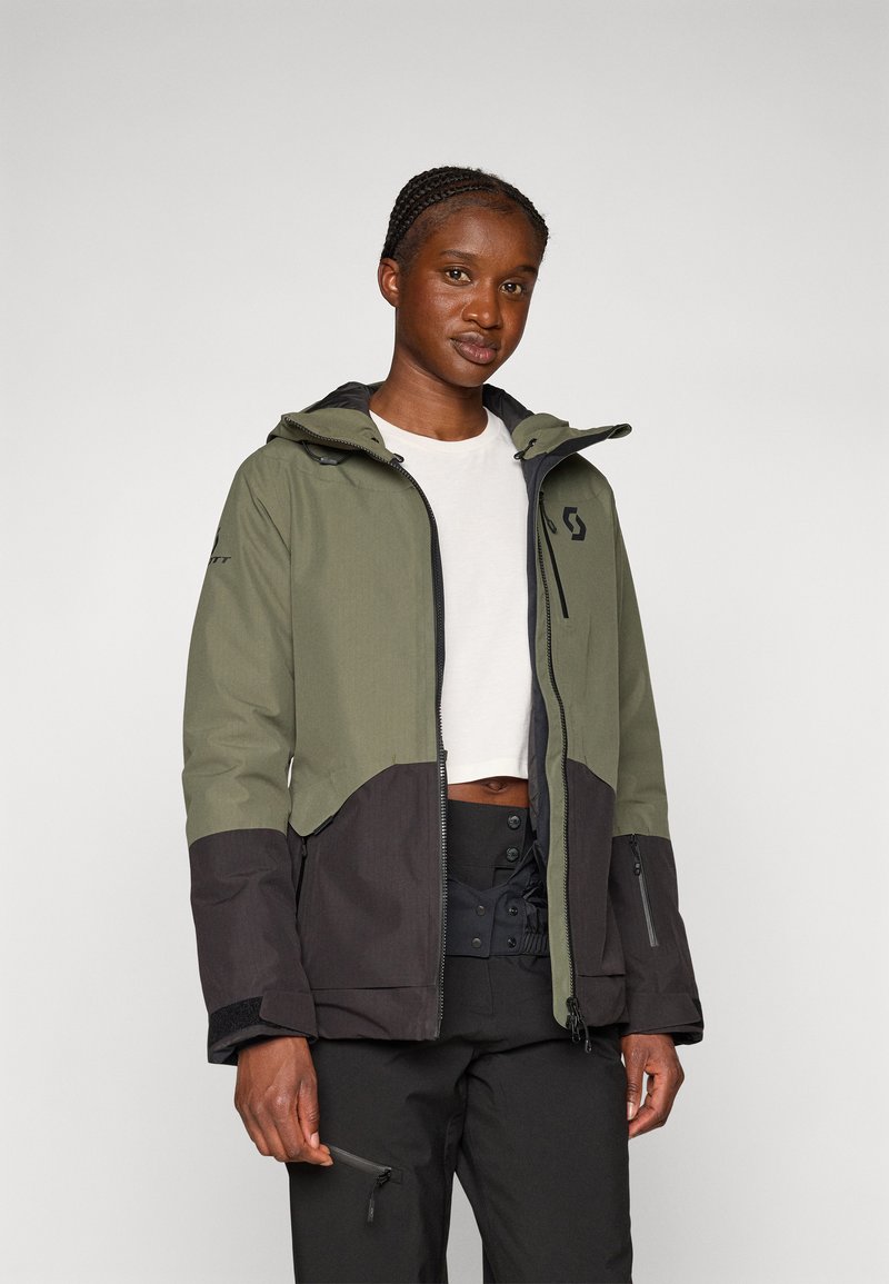 Grüne und schwarze wasserdichte Jacke mit Kapuze, Reißverschlusstaschen und kontrastierendem Paneeldesign. Hergestellt aus strukturiertem Stoff.