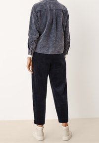 Camicia di denim in un blu sbiadito con una vestibilità rilassata, maniche lunghe e polsini con bottoni, abbinata a pantaloni in velluto a coste blu navy e sneakers chiare.