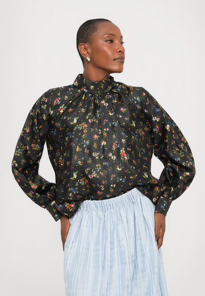 Blusa nera floreale con collo alto, maniche lunghe e dettagli plissettati. Il tessuto ha una leggera lucentezza con motivi floreali multicolori.