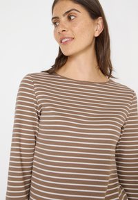 Braun und weiß gestreiftes Langarmoberteil mit rundem Ausschnitt. Der Stoff wirkt weich mit einer gerippten Textur. Minimalistisches Design, taillierte Silhouette.