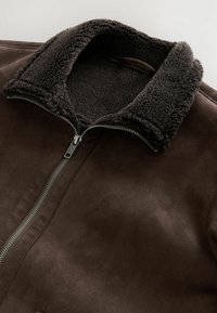 Braune Fake-Suede-Jacke mit einem flauschigen, dunklen Fellkragen und einem Metallreißverschluss, die über eine glatte Textur und ein sauberes Design verfügt.