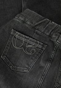 Schwarze Jeans aus Denim mit strukturierter Oberfläche, ausgestattet mit einer Gesäßtasche, die mit grauem Gestick in einem spiralförmigen Design verziert ist.