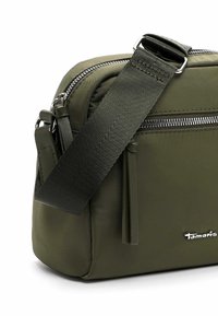 Grüne Nylon-Schultertasche mit einer Reißverschlusstasche auf der Vorderseite, glatter Textur, verstellbarem Riemen und einem silbernen Logo-Detail an der Seite.