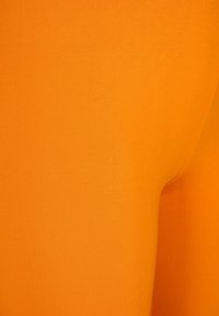 Collants orange en tissu lisse et extensible avec un design ajusté. Aucun motif visible ni détails matériels.