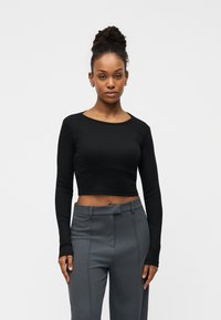 Μαύρο μακρυμάνικο crop top από ριμπ ύφασμα, με στρογγυλή λαιμόκοψη και εφαρμοστά μανίκια, σε συνδυασμό με γκρι ψηλόμεσο παντελόνι.