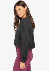 Black cropped long-sleeve top with a relaxed fit and wide sleeves, paired with plum corduroy pants for a contrasting texture.