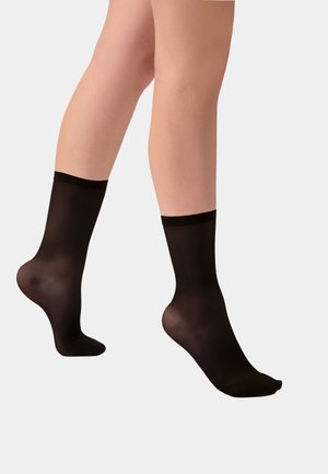 Legs wearing sheer black ankle socks against a light gray background, showing sock fit and size.