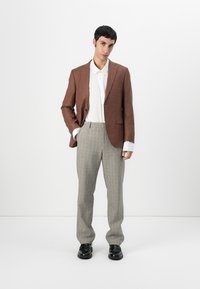 Hnedý blejzer cez bielu košeľu, skombinovaný s károvanými nohavicami. Hladká tkanina, strih na mieru, elegantné čierne topánky, stojac na rovnom pozadí.