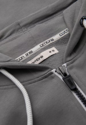 Grauer Zip-Hoodie aus Baumwolle mit Kapuze und Kordelzug, kontrastierendem weißen Reißverschluss und Markenlabel in Größe M. Weicher Stoff.