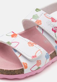 Sandalias blancas con patrones florales coloridos, correas ajustables y una plantilla de corcho. La suela es rosa y tiene una superficie texturizada para mayor agarre.