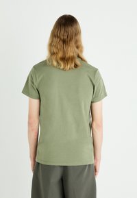 Oliwkowa bawełniana koszulka z krótkim rękawem, okrągłym dekoltem i gładką fakturą. Tył ma prosty wzór bez nadruków.