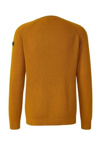 Musztardowożółty sweter z dzianiny z długim rękawem, o prążkowanej fakturze, z okrągłym dekoltem i małą czarną naszywką na lewym rękawie.