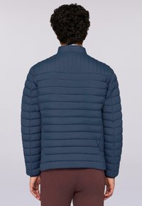 Mörkblå puffjacka med horisontell quiltad design, ståkrage och sidofickor. Slät textur och lätt material.