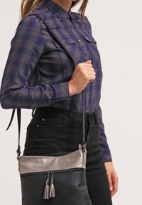 Borsa a tracolla nera e metallica con una texture liscia, dotata di due scomparti con zip e dettagli con frange. Inclusa tracolla regolabile.