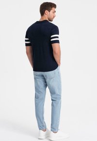 Marinblå polo med vita ränder på ärmarna, kroppsnära passform, tillsammans med ljusblå jeans och vita sneakers. Enkel, avslappnad look.