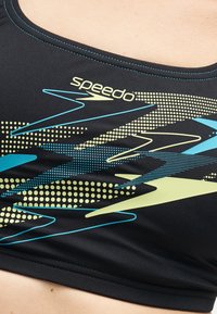 Κοντινό ενός μαυρου μπικίνι Speedo με μοτίβα μπλε, κίτρινου και τιρκουάζ κεραυνού και διακοσμητικά πουά.
