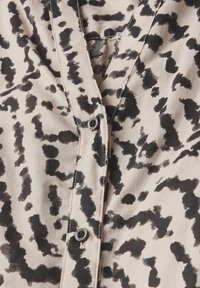 Camicia button-up nera e beige con un motivo astratto a macchie, realizzata in tessuto morbido, con scollatura a V e discreto dettaglio hardware.