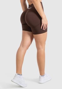 Bruine sportshorts met een hoge taille, textuurdetails en een aansluitend ontwerp, gecombineerd met witte sportschoenen.
