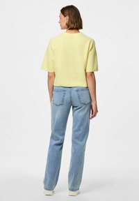 Dzeltena teksturēta īsām piedurknēm jaka apvienota ar gaiši ziliem taisniem džinsiem. Apģērbs ietver vienkāršu kakla izgriezumu un aizmugurējās kabatas džinsos.