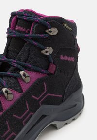 Melni pārgājienu zābaki ar rozā akcentiem, zamšāda un sintētiska augšdaļa, teksturēts raksts, metāla acis un izturīga gumijas zole. Ietver Gore-Tex zīmolu.