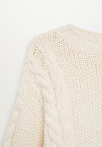 Pull en maille épaisse de couleur crème avec détail torsadé le long des manches et points texturés sur le corps.