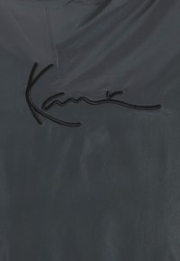 Tessuto nero con una texture liscia, caratterizzato da un prominente logo ricamato in filo nero. Design semplice ed elegante senza ulteriori decorazioni.
