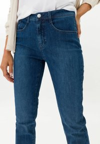 Dunkelblaue Denim-Jeans im Slim-Fit, mit Fronttaschen, Reißverschluss und Metallknopfverschluss. Leichte Ausbleichungen und subtile Texturdetails.