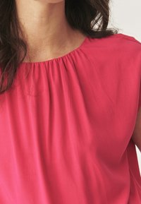 Lys pink bluse med rund halsudskæring og rynkedetaljer ved yoken. Fremstillet af glat, letvægtsstof med en afslappet pasform.