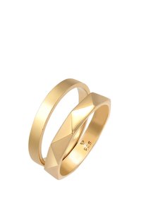 Deux bagues en or empilées. L'une est une bande lisse et polie ; l'autre présente un design géométrique facetté. Les deux sont marquées "925".