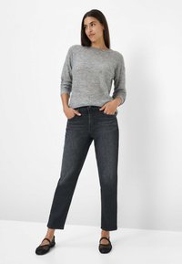 Pull en maille gris avec un col rond, associé à un jean droit bleu marine et des ballerines noires tissées, les mains dans les poches.