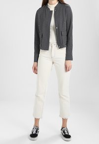 Granatowo-biała kurtka w paski z okrągłym dekoltem, dwie kieszenie z przodu; zestawiona z białymi, krótko przyciętymi jeansami i czarnymi sneakersami.