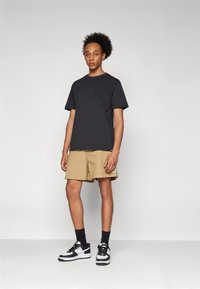 Sort bomulds T-shirt med rund halsudskæring, khaki shorts med afslappet pasform og sort-hvide sneakers. Enkel design, ingen synlige mønstre.