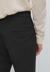 Pantaloni neri realizzati in tessuto liscio; presentano una vestibilità slim, passanti per cintura e una piccola tasca posteriore orizzontale senza hardware visibile.