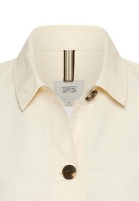 Lys beige skjorte med krave og knaplukning, der har en lodret stribet detalje på kraven. Glat bomuldsstruktur.