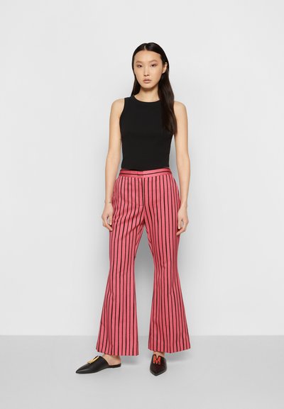Calças flare listradas em rosa, tecido texturizado, cintura alta, combinadas com uma camisola preta ajustada e sapatos slip-on pretos com uma ornamentação.