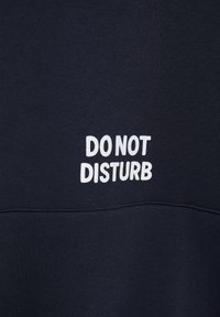 Tissu noir avec texte blanc centré disant « Ne pas déranger » en lettres majuscules en gras.