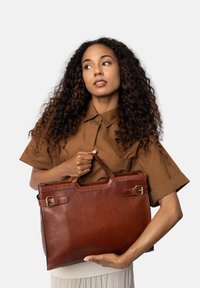 Brun læder tote taske med to håndtag, en flad rektangulær form, spænde detaljer og glat tekstur. Fint syning langs kanterne.