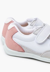 Zapatillas blancas con una mezcla de superficies lisas y texturizadas. Presentan acentos en rosa claro y gris, correa de velcro y un diseño redondeado.