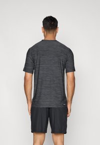 Lyhythihainen urheilupaita tummanharmaana, jossa on hienovarainen vaakaraidoitus, yhdistettynä mustiin shortseihin. Asusteet näyttävät rentoilta ja niissä on sileä tekstuuri.