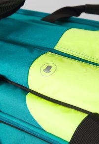Mėlynos spalvos kuprinė su tekstūruotu paviršiumi, išsiskirianti ryškiu geltonu skyriumi ir subtiliu logotipo akcentu. Juodi užtrauktukai ir diržai papildo jos dizainą.
