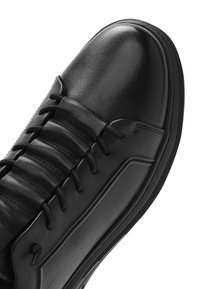 Sneaker in pelle nera con una superficie liscia, caratterizzato da dettagli a coste e lacci tradizionali. Punta arrotondata e suola in gomma nera.