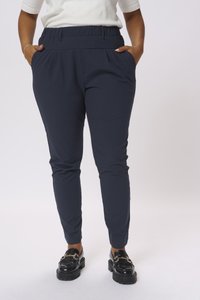 Pantaloni stretch blu navy con una vita alta ed elastica, tasche laterali, gambe affusolate e una texture liscia. Abbinati a mocassini neri con plateau.