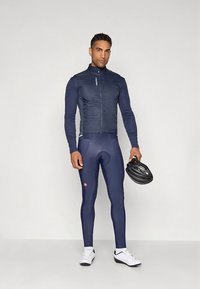 Marineblå sykkelantrekk med en tettsittende jakke med glidelås og tights. Tilbehør inkluderer en svart hjelm. Laget av elastisk, lett stoff.