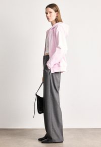 Ružový mikina s kapucňou, šedé široké nohavice s pásikmi, čierna taška, čierne topánky. Jednoduchý dizajn, pohodlná látka a voľný strih.