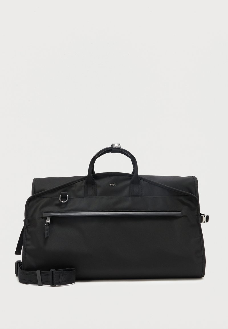 Μαύρη τσάντα BOSS τύπου duffel με χερούλια στο πάνω μέρος, μπροστινή τσέπη με φερμουάρ, ρυθμιζόμενο λουρί ώμου και ασημένιο μεταλλικό εξάρτημα σε λευκό φόντο.