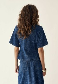 Top in denim blu a maniche corte con un motivo testurizzato, caratterizzato da una vestibilità comoda e un orlo dritto, abbinato a una gonna coordinata.